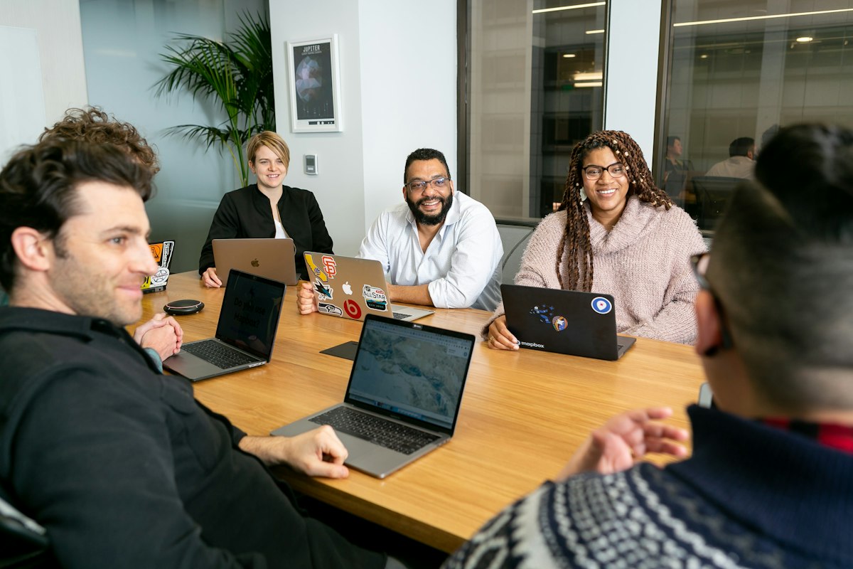 Sales team meeting around a table with laptops to compare B2B business database options